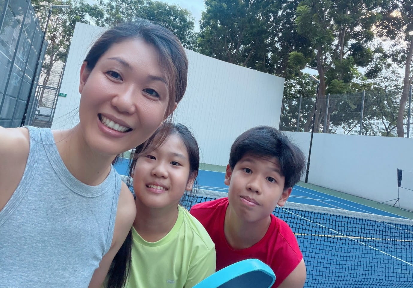 A woman and two children posing for a selfie at an outdoor court.